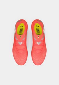 Jasnoróżowe neonowe buty piłkarskie o smukłym designie, teksturowanej cholewce, odblaskowych akcentach oraz żółtej wkładce z kodem QR.