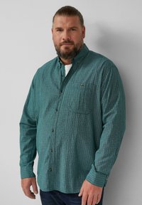 Turquoise blokpatroond blouse met knopen, een zak, lange mouwen en een kraag. De stof lijkt textuur te hebben en is lichtgewicht.