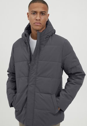 Gray hooded puffer jacket with a zip front, horizontal quilted design, side pockets, and a soft texture. Worn over a white T-shirt.
