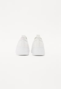 Sneaker bianche con tomaia in pelle liscia, suola bianca spessa e linguetta sul retro. Design semplice con dettagli di cucitura leggera lungo le cuciture.