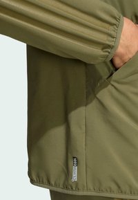 Olive green jacket with textured fabric, elastic cuffs, and a side pocket. Features a "climacool" label on the hem.