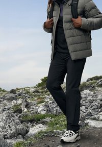 Grå pufferjakke med struktureret design, et sort fleece lag under, sorte bukser og hvide sportssko med kontrastfarver.