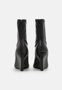 Bottines en cuir noir avec une pointe et un haut talon aiguille. Dotées d'une fermeture éclair à l'arrière et d'un design froncé en haut pour un ajustement confortable.