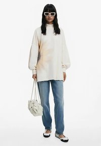 Üle suurusega kreemjas pusa gradiente mustriga, kulunud äärega, sinised teksad, mustad ja valged madalad kingad ning tekstuurse valge käekotiga.