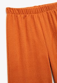 Orange tekstureret stofbukser med elastisk talje, der har lodrette linjer og en afslappet pasform. Blød, let fuzzy overflade.