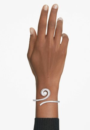 Silberne Spiralarmband mit strukturiertem Finish und einem weißen Perlenakzent. Tragen auf einer Hand mit natürlichen Nägeln vor einem weißen Hintergrund.