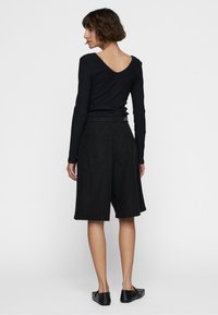 Zwarte lange mouw ribtop met een V-hals en zwarte denimshorts met een relaxte pasvorm en elastische tailleband. Zwarte instappers.