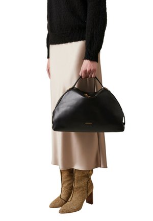 Sac à main en cuir noir avec ferrures dorées, dessus arrondi et doubles poignées, tenu par une personne portant une jupe en satin crème et des bottes à motifs.