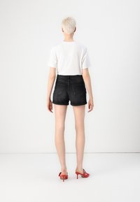 Shorts di denim neri con orli arrotolati, vita alta e tasche posteriori, abbinati a una t-shirt bianca semplice e sandali con tacco rossi.