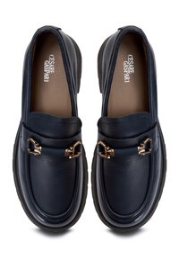 Mocassins en cuir noir avec détail en métal doré en forme de mors de cheval et semelle intérieure griffée, vus de dessus sur fond blanc.