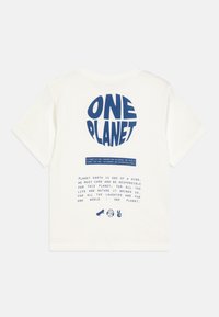 Kremfarget t-skjorte med kort arm som har blå sirkulær tekst "ONE PLANET" og ytterligere tekst under. Laget av bomull, avslappet passform, uten mønstre.