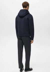 Sudadera con capucha de color azul marino con un acabado texturizado, combinada con pantalones a medida de color gris oscuro y zapatos negros. Enfoque en líneas limpias y diseño minimalista.