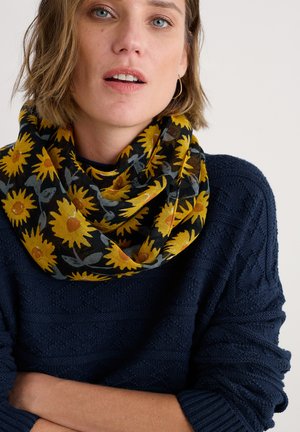 Écharpe à motifs de tournesols jaunes sur fond noir, en tissu léger, enroulée autour du cou, associée à un pull en marine texturé.