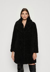 Cappotto nero e soffice con un ampio colletto, maniche lunghe e una vestibilità rilassata. Realizzato in un morbido tessuto texturizzato con chiusura a bottoni nascosta.