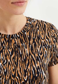 Brun- och svartrandig skjorta med rund halsringning, tillverkad av mjukt tyg, med ett djärvt abstrakt mönster och korta Ärm.