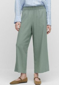 Lichtgroene wijde broek met een elastische taille, gemaakt van zachte stof, gecombineerd met een blauw-wit gestreept shirt en bruine ballerina's.