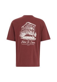 Mørkerød bomulds T-shirt med en hvid grafisk illustration af en bygning med teksten "Hotel Il Sogno" og detaljer nedenfor. Korte ærmer, afslappet pasform.