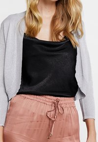 Silver glittrig cardigan över en svart satin cami, kombinerad med en mjuk, dammig rosa plisségrynad kjol med dragsko i midjan.