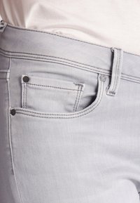 Jeans de mezclilla gris claro con un diseño clásico de cinco bolsillos, costuras sutiles y detalles de metal en los bolsillos.