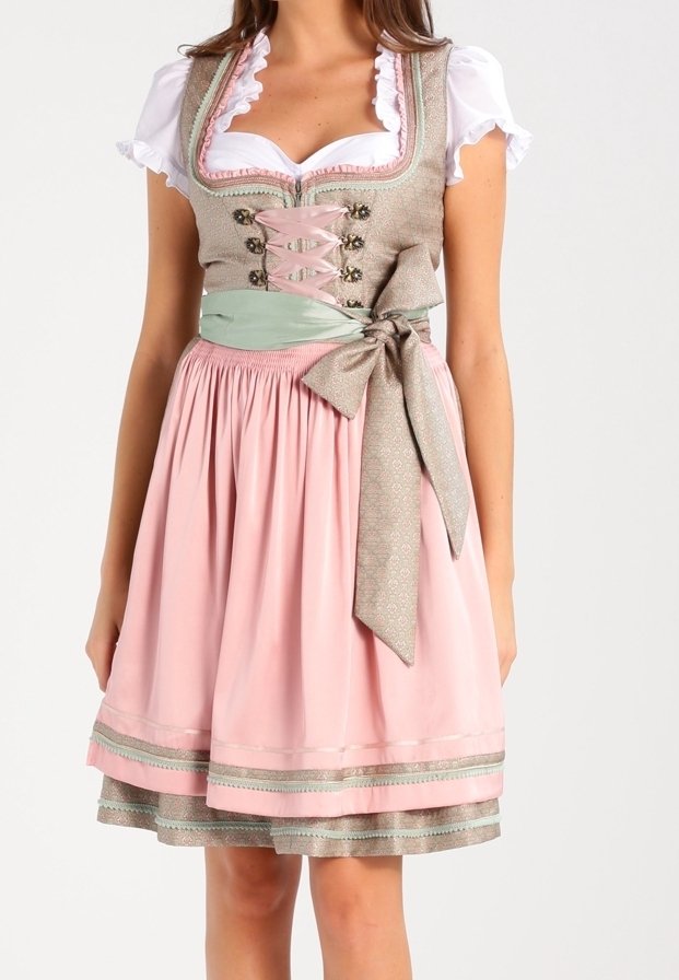 Femme portant une robe traditionnelle dirndl rose et beige avec une blouse blanche, un corsage lacé et un grand nœud noué à la taille.