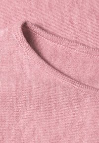 Tissu tricoté rose doux avec un bord plié montrant une couture fine et une texture lisse.