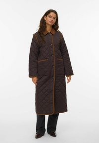 Cappotto lungo imbottito di colore marrone scuro con un motivo a rombi, colletto marrone, chiusura con bottoni e tasche laterali, con rifiniture a contrasto di colore marrone.