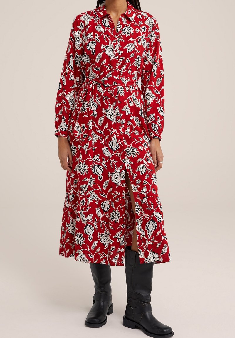 Röd blommig klänning med vita mönster, långa ärmar, knappkrage och en slits framtill. Matchas med knähöga svarta stövlar.