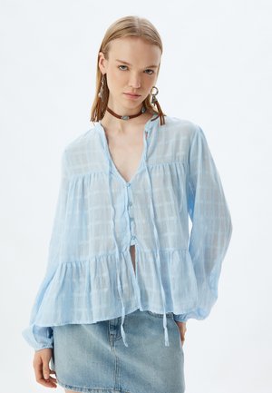 Light blue cotton blouse with a checkered pattern, v-neck, button front, and peplum design. Features long sleeves and drawstring accents.