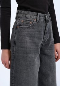 Hochtaillierte graue Denim-Jeans mit geradem Bein, ausgestattet mit kupferfarbenen Nieten, Seitentaschen und einer subtilen Textur.