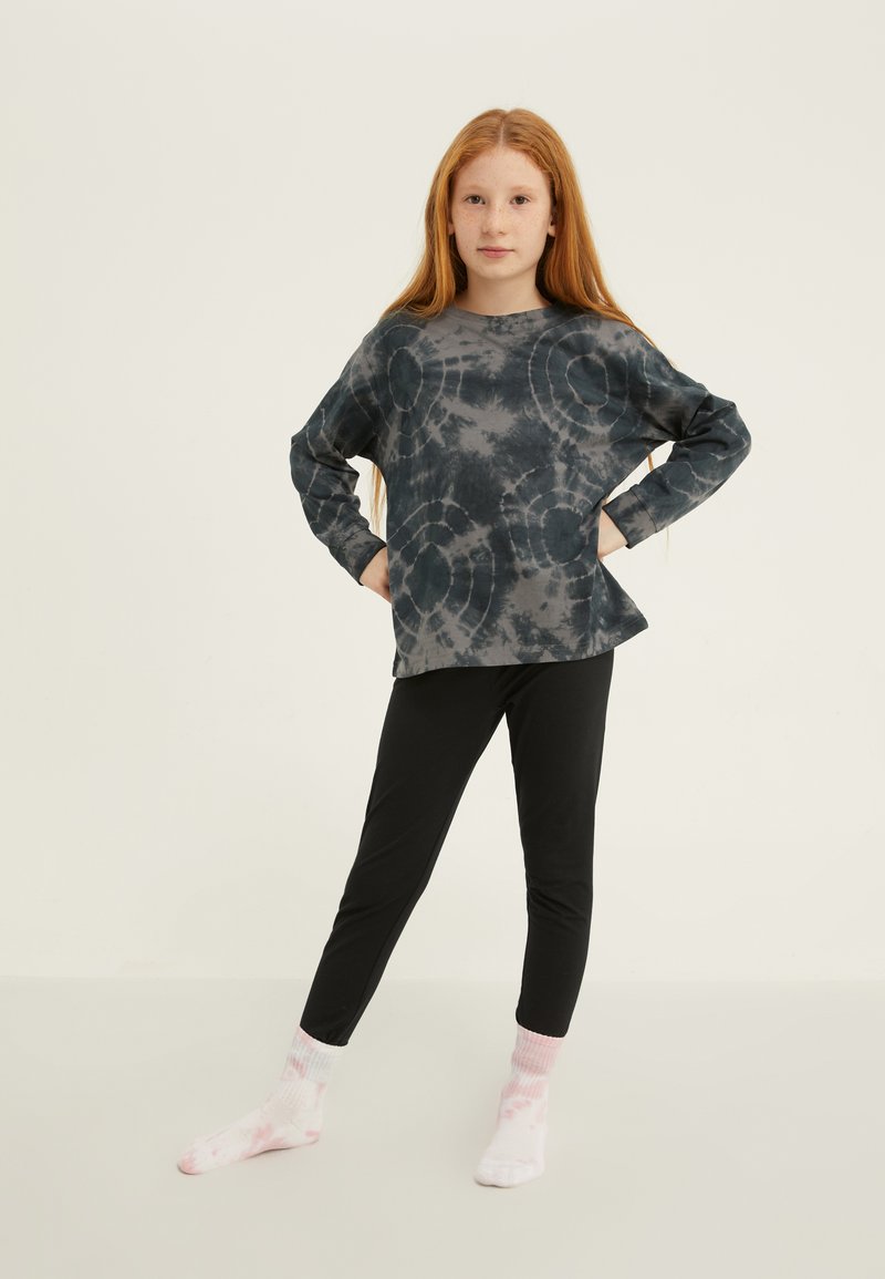 Dlhý rukáv tričko s batikovým vzorom v tmavo šedej farbe s kruhovými vzormi, kombinované s čiernymi legínami a ponožkami s ružovými a bielymi vzormi.