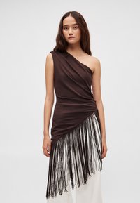 Bruine asymmetrische top gemaakt van zachte stof met een gedrapeerd ontwerp, voorzien van lange zwarte franjes aan de zoom.