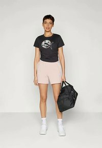 Čierne tričko s krátkym rukávom s farebným logom hory, spárované s ružovými šortkami a bielymi teniskami; drží čiernu športovú tašku.