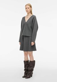 Siva volnena mešanica prevelika majica z V-izrezom, v kombinaciji z ujemajočo se sivo razširjeno krilo. Dopolnjujejo jo rjave usnjene škornje do kolen.