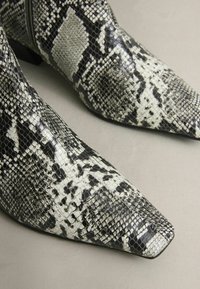 Fekete és fehér kígyómintás, hegyes orrú bokacsizma, amely textúrált felülettel rendelkezik, jól megkülönböztethető mintázatokkal és alacsony blokk sarkú.