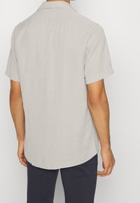 Camicia grigia chiaro a maniche corte con colletto, texture liscia e orlo curvo. Presenta una cucitura posteriore dritta e maniche arrotolate.