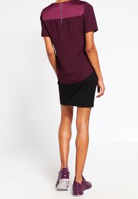 Bordeaux kortärmad topp med en satinpanel, parat med en svart kjol. Bärs med lila träningsskor. Har en dragkedjedetalj bak.