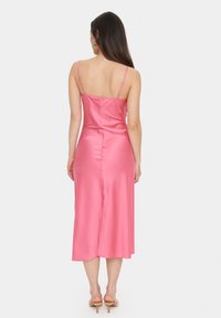 Robe midi en satin rose avec des bretelles fines, présentant un design élégant et une fente discrète dans le dos, mettant en valeur une texture lisse et brillante.