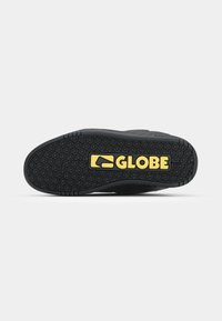 Czarna podeszwa od buta do skate'a z teksturowanej gumy, z wzorzystym uchwytem i wyraźnym żółtym logo "GLOBE". Wygięty design z trwałych materiałów.