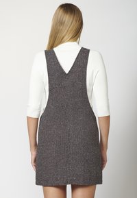Grå och vit rutig hängselklänning med V-bakdesign, tillverkad av textilier med struktur, med en figursydd silhuett och ärmlös skärning.
