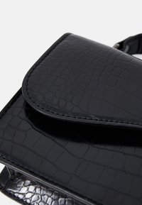 Sac à main noir avec un motif en relief imitant les reptiles. Fini glossy, fermeture à rabat arrondi et couture visible. Design compact avec une esthétique épurée.