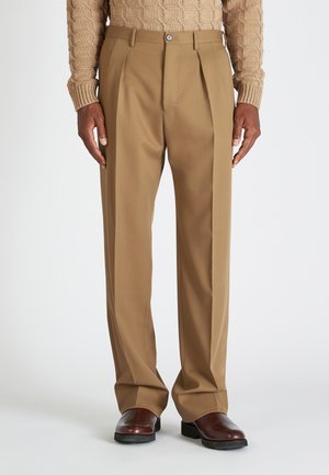Beige geplaatste broek met een getailleerde pasvorm, gemaakt van een gladde stof. Voorzien van een knoopsluiting en zakken, gecombineerd met donkere schoenen.