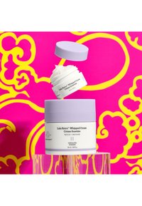 Lala Retro Whipped Cream jar in white and lavender with a textured lid, topped by a smaller container; vibrant pink and yellow background.