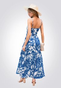 Robe maxi bleue à fleurs avec bretelles spaghetti, dotée d'un dos smocké, d'un tissu fluide et d'une texture légère. Associée à un chapeau en paille.