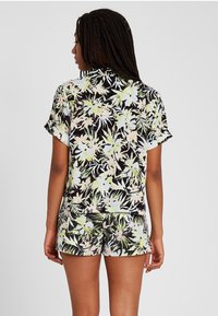 Short-sleeve tropical floral top and matching shorts in black, featuring large pastel flowers and green leaves, made from a lightweight fabric.