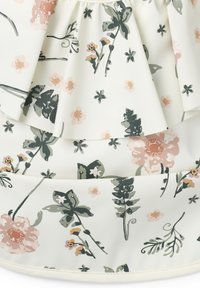 Blommigt bomullstyg med en krämfärgad bakgrund, prytt med lager av volanger, rosa och gröna botaniska mönster samt en mjuk textur.
