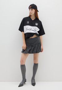 Jersey de gran tamaño en blanco y negro con un logo, combinado con una falda gris con volantes, calcetas grises hasta la rodilla y tacones negros con tachuelas.