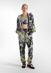 Kukallinen aktiivivaatteiden setti, jossa on lyhyt toppi ja väljät housut. Värit ovat musta, valkoinen ja kirkkaan keltaiset korostukset.