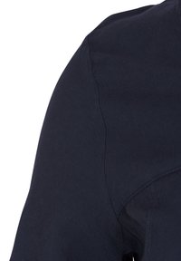 Detailní záběr tmavě modré látky s viditelnými švy a prošíváním v oblasti ramene oděvu.