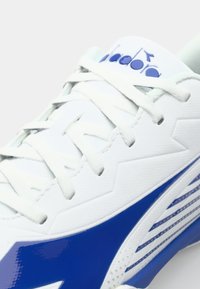White athletic shoe with blue accents, featuring a textured upper, zigzag pattern, and flat laces. Notable logo on the tongue.