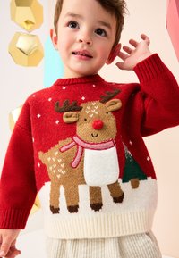 Pull rouge en maille avec motif de renne, section inférieure blanche, poignets côtelés et accents texturés. Idéal pour les tenues festives.